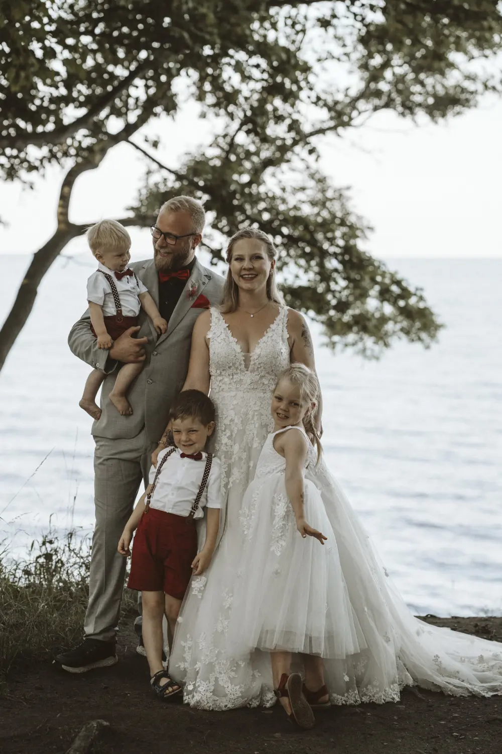 Frisch verheiratetes Paar mit Kindern beim After-Wedding-Shooting am Katharinhof auf Fehmarn. Naturkulisse mit Bäumen, Wiese und Ostsee-Flair im Hintergrund